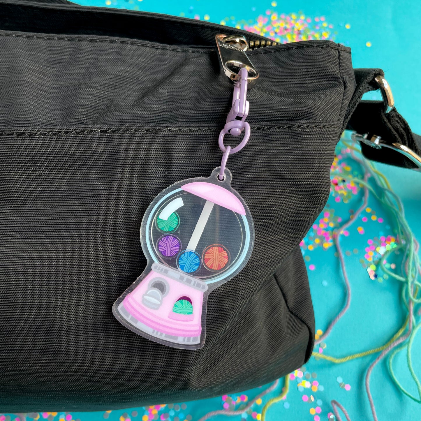 A pink gumball machine shaped keychain attached to the zipper of a black purse. 
