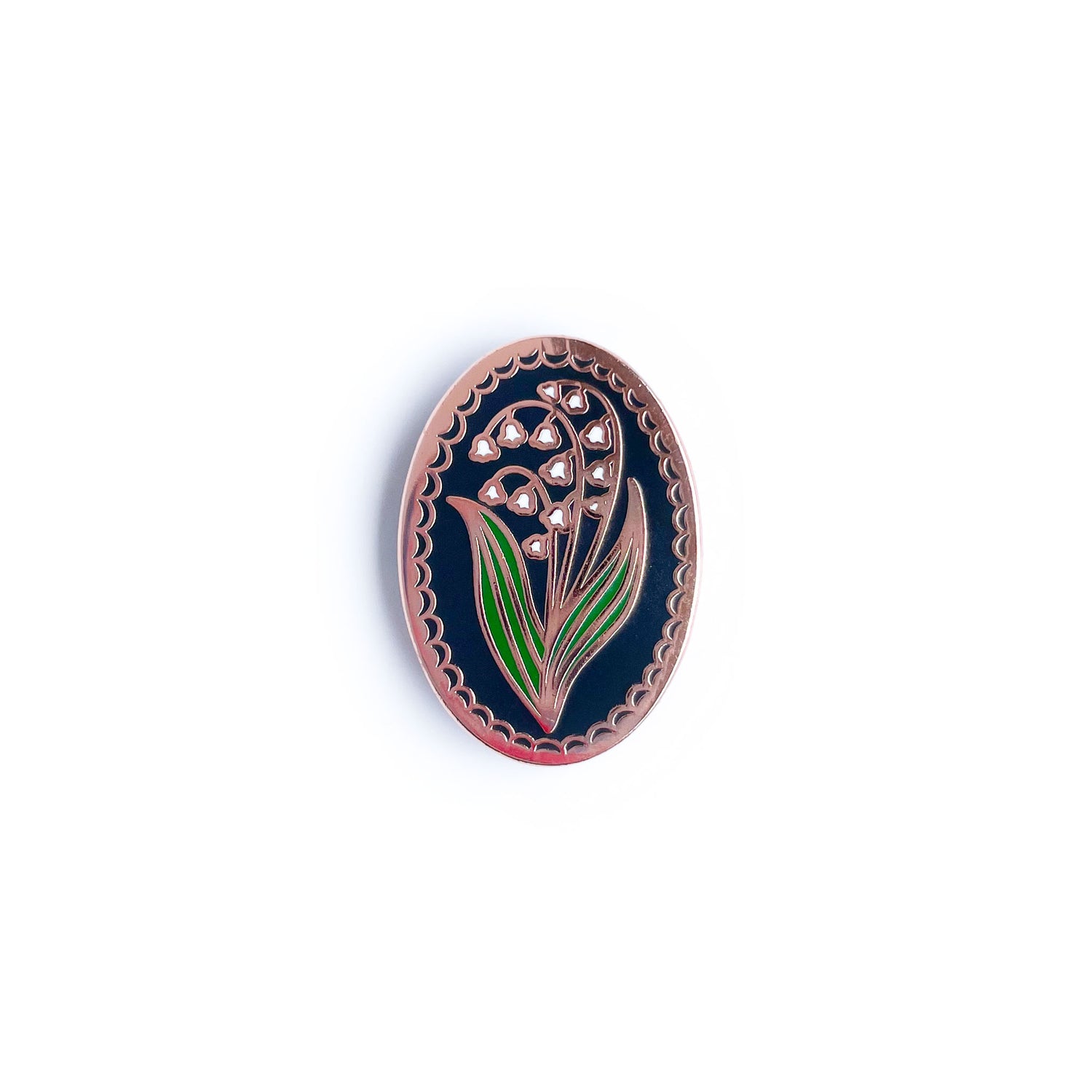 An enamel pin shaped like an oval with a lily of the valley in it.