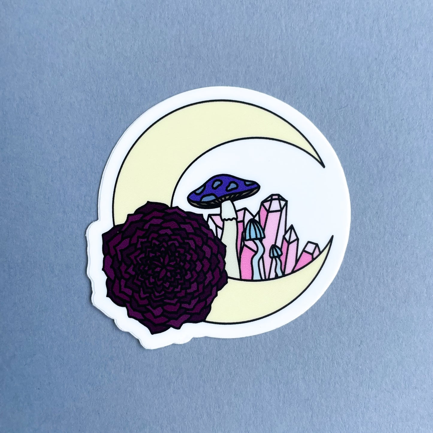 A crescent moon with crystals and mushrooms inside it on a grey background.