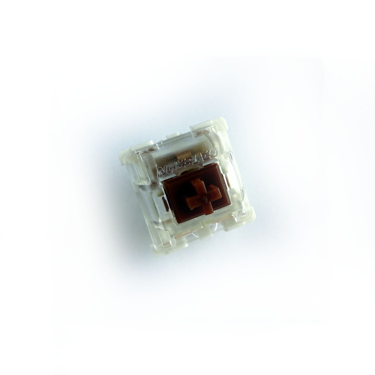 A tactile keyboard switch on a white background. The switch component is brown, the bottom of the casing is white, and the top of the casing is clear with the word "GATERON" imprinted into it.
