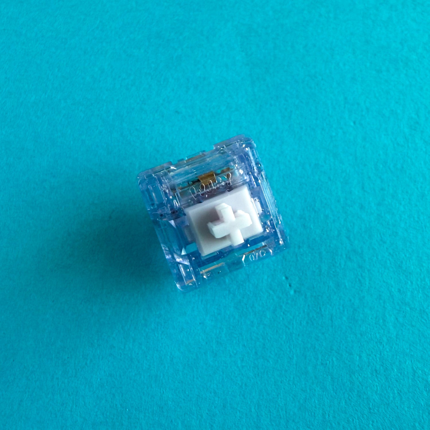 A linear keyboard switch on a blue background. The switch component is white, and the casing is a translucent purple with sparkles.