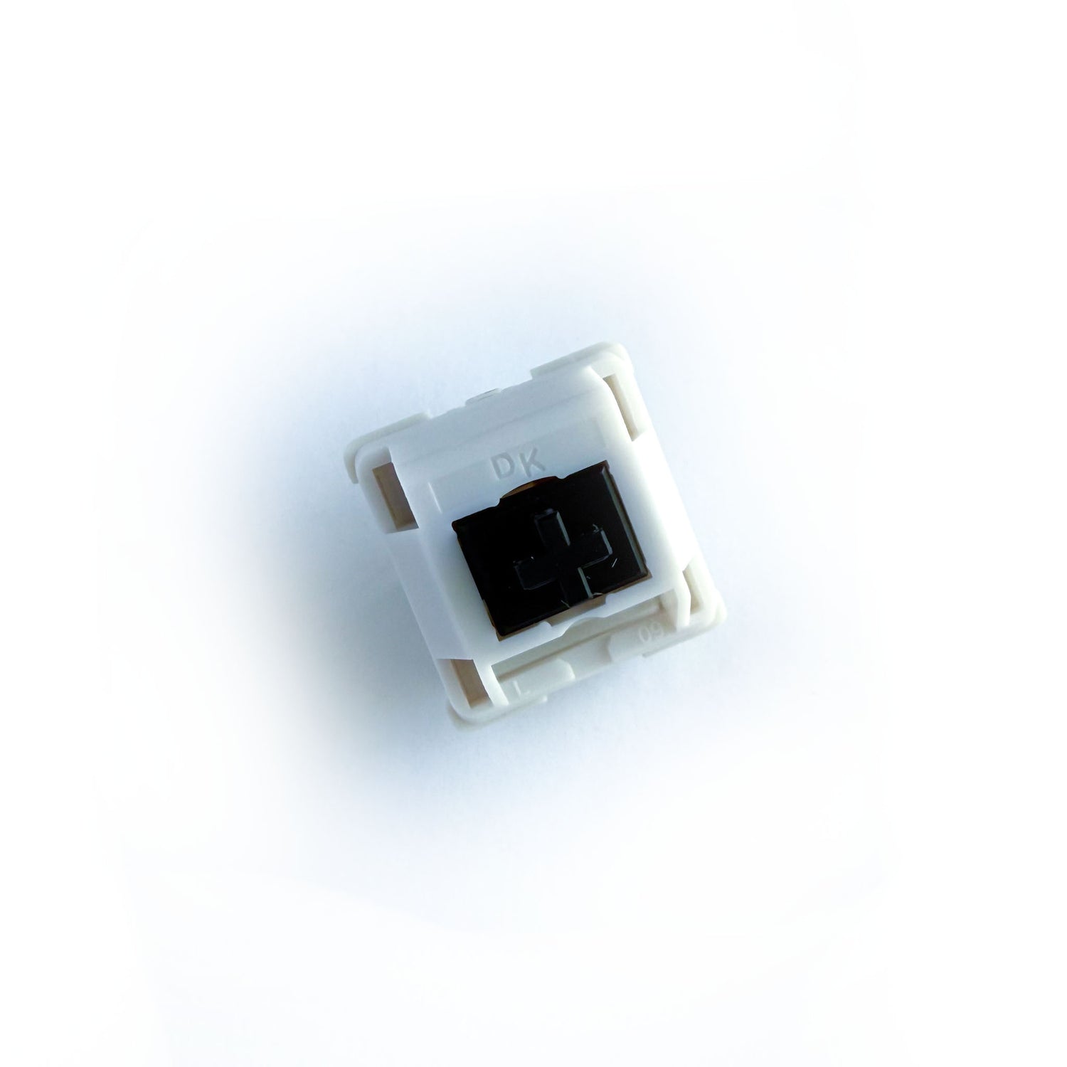 A tactile keyboard switch on a white background. The switch component is black, and the casing is white with the letters "DK" imprinted into it.