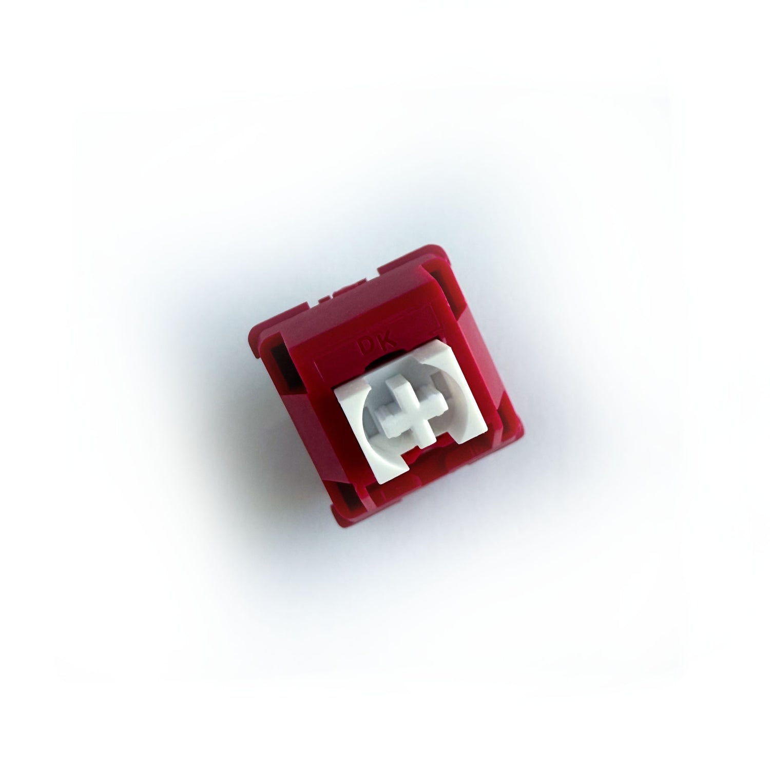 A tactile keyboard switch on a white background. The switch component is white, and the casing is a deep red with the letters "DK" imprinted into it.
