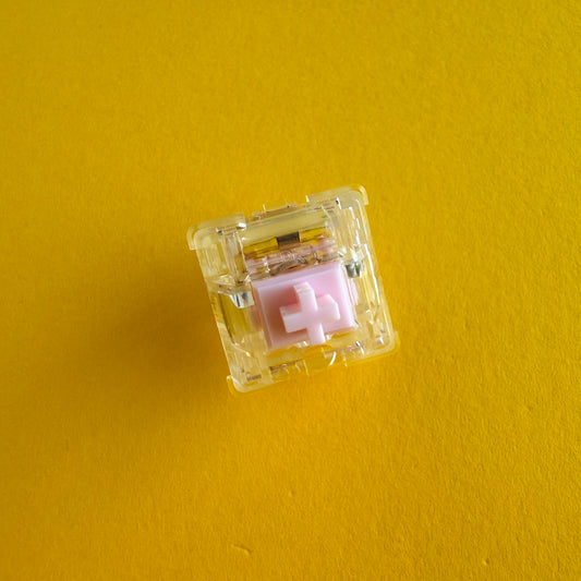 A tactile keyboard switch on a yellow background. The switch component is light pink, the casing is clear. 