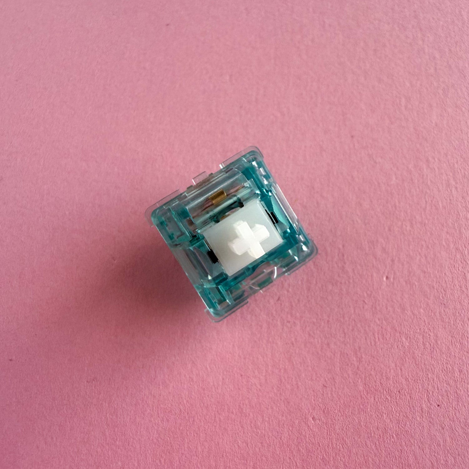A tactile keyboard switch on a pink background. The switch component is white, and the casing is a translucent blue.