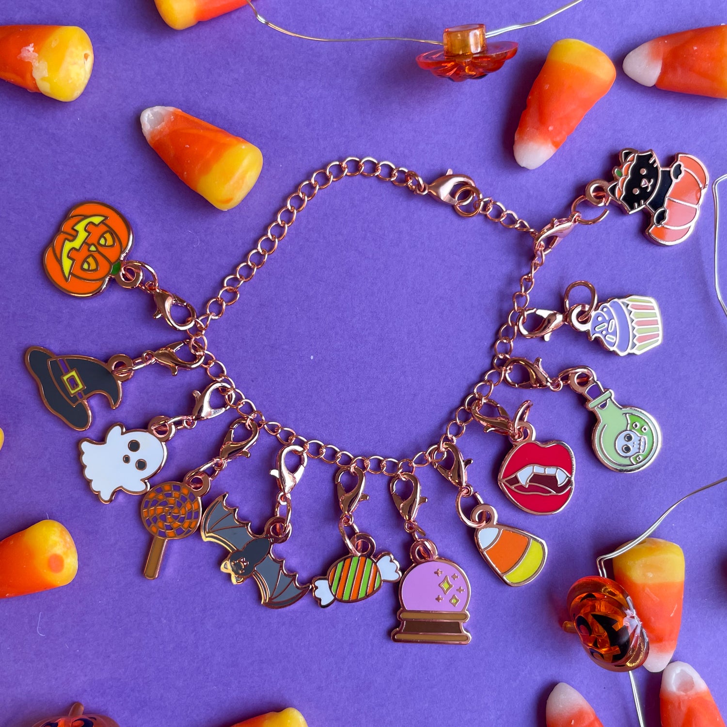 A rose gold colored charm bracelet with 12 lobster claw clasp charms shaped like various halloween items.