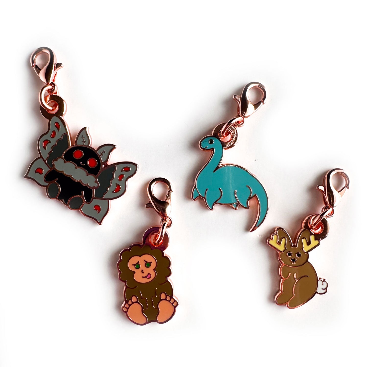 A set of four enamel charms in the shape of cryptids in the same cute illustration style, there is a Mothman, Bigfoot, Nessie, and jackalope charm. The charms all have lobster claw clasps