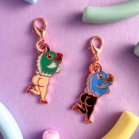 Two charms with lobster claw clasps shaped like reverse mermaids, fish on top and naked lady legs on the bottom with cheeks out and high heels on. One mermaid has a teal fish head with red lips and white legs and the other has a blue fish head with coral lips and black legs. The charms are on a lavender background with beads around them.