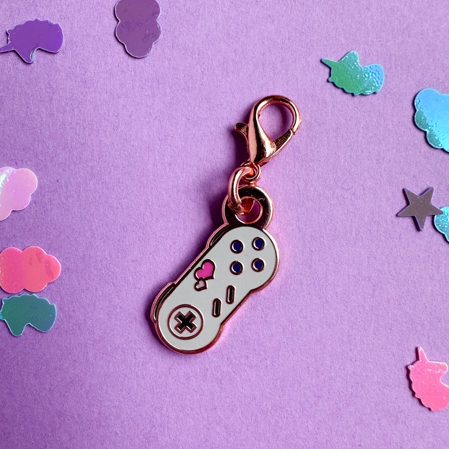 A lobster claw clasp charm shaped like a Super Nintendo controller with hearts on it. The charm is on a lavender confetti background.