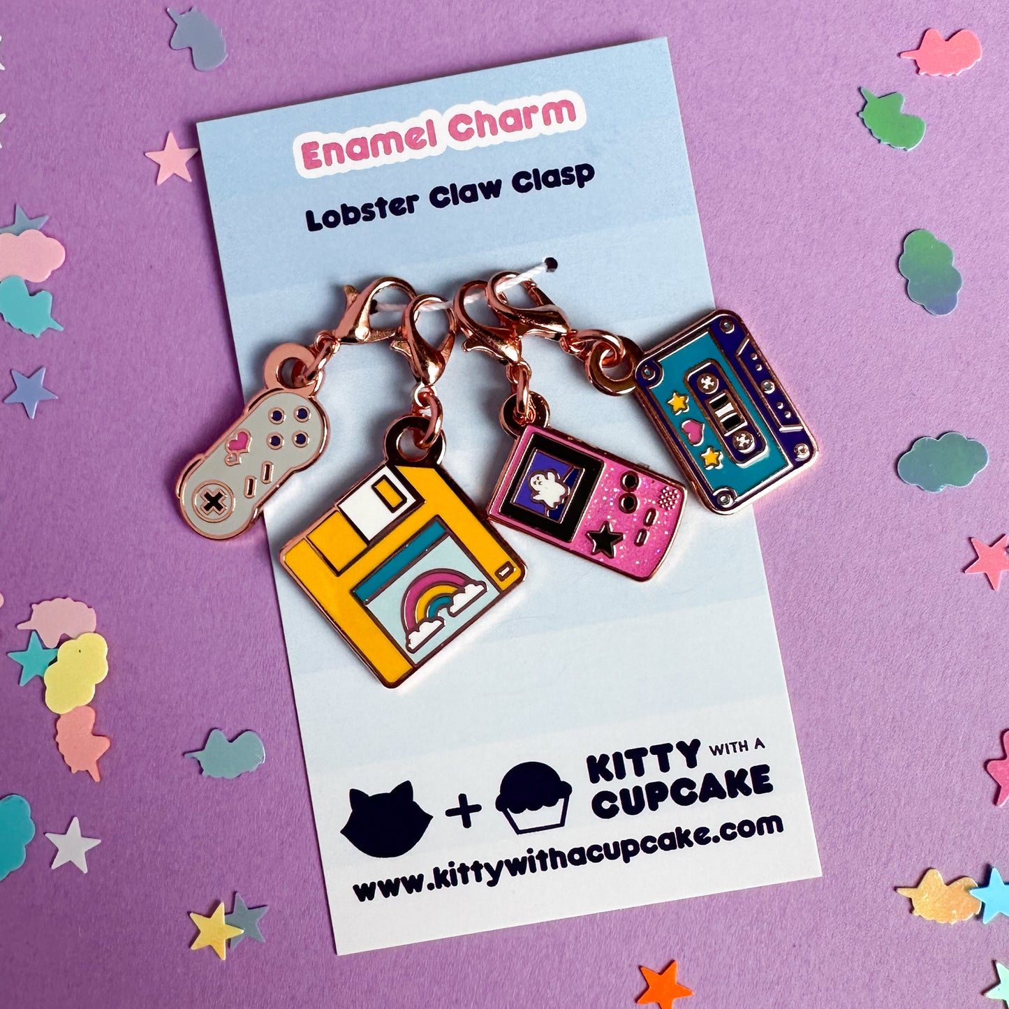 A four pack of charms packaged on a blue card. The charms are shaped like a game console controller, floppy disk, gameboy, and a cassette tape. 