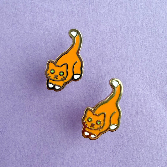 Product photo of the Orange Cat Earrings. This cat has green eyes and an orange body with a white tail tip and feet. There are two earrings displayed diagonal from each other. The earrings are resting against a purple background.