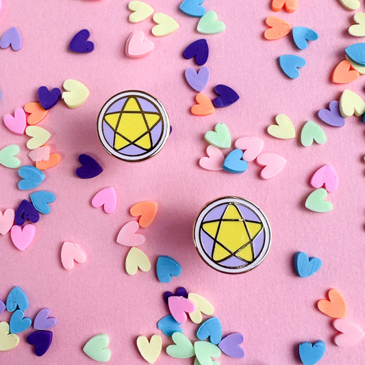 Stud earrings in the shape of pentacles with pastel pink and lavender coloring and yellow stars on top of a pink paper background with pastel heart confetti on it. 
