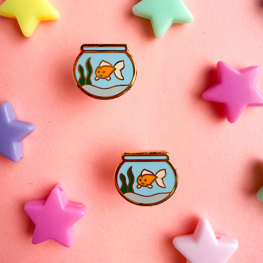 Goldfish bowl shaped enamel earrings on a pink background with star beads around them. 