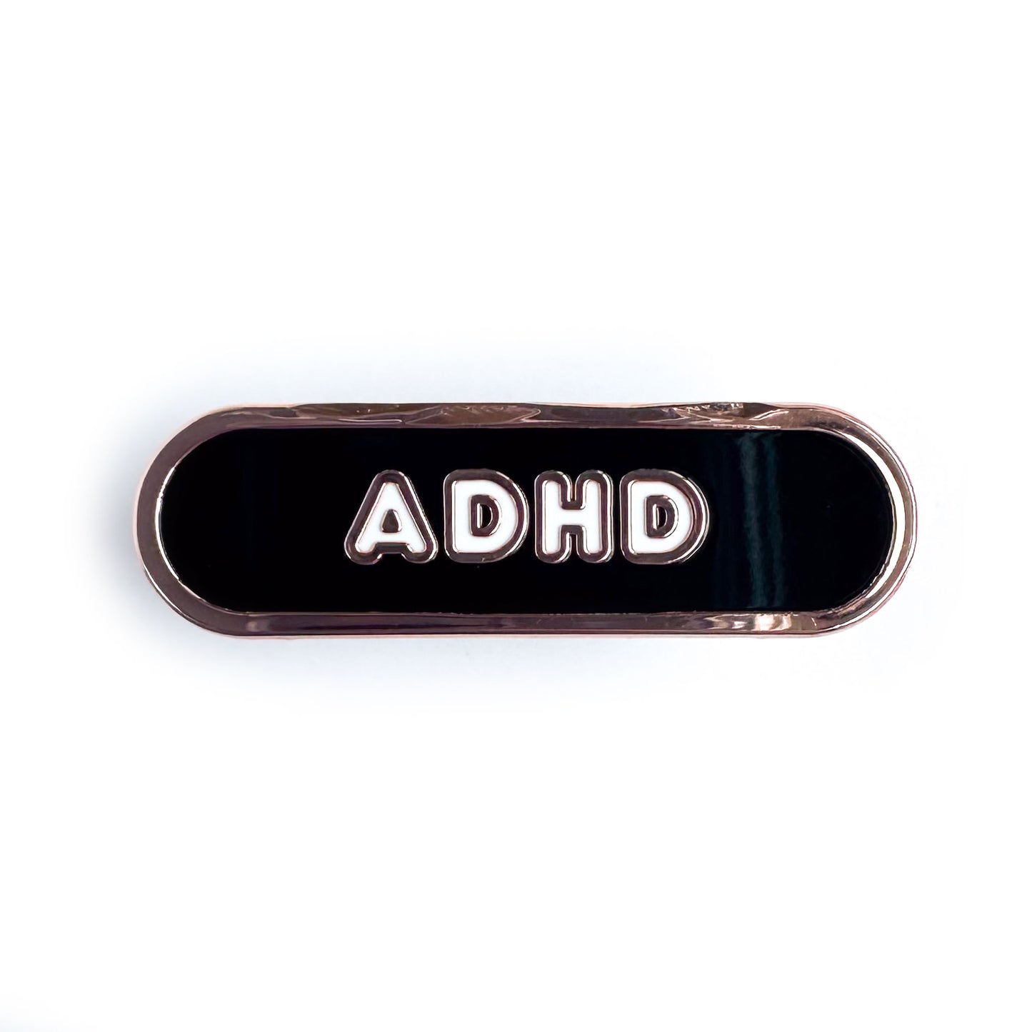 A black capsule shaped enamel pin with the letters ADHD on it in white bubble letters.