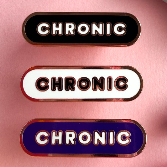 Three bandaid shaped pins with the text CHRONIC in bubble letters. Top one black with white text, the next is white with black text, and the last is violet with white text. The pins are on a pink background.