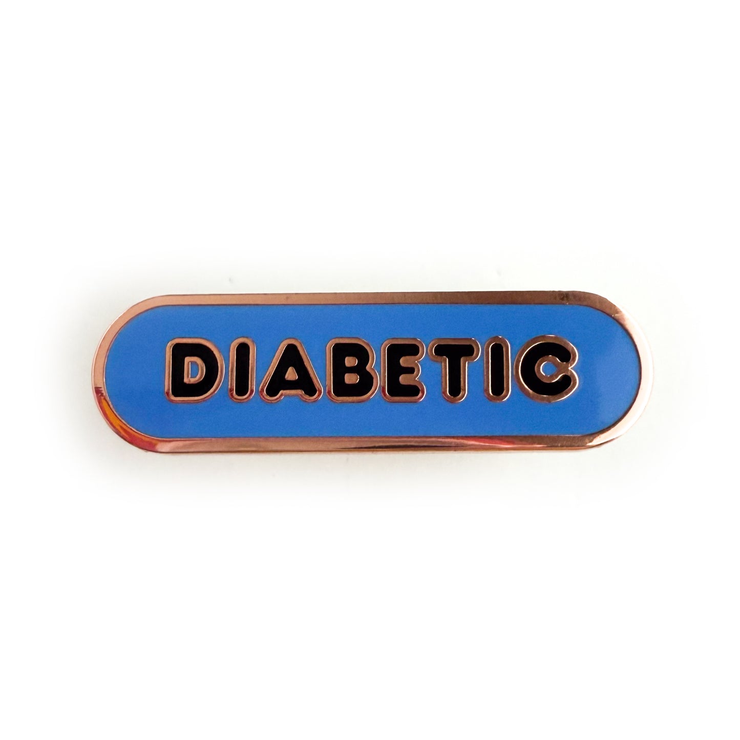 A bandaid shaped pin with the text DIABETIC in bubble letters. The background is cornflower blue and the text is black.