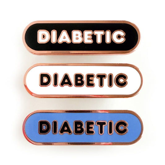 Three bandaid shaped pins with the text DIABETIC in bubble letters. Top one black with white text, the next is white with black text, and the last is cornflower blue with black text.