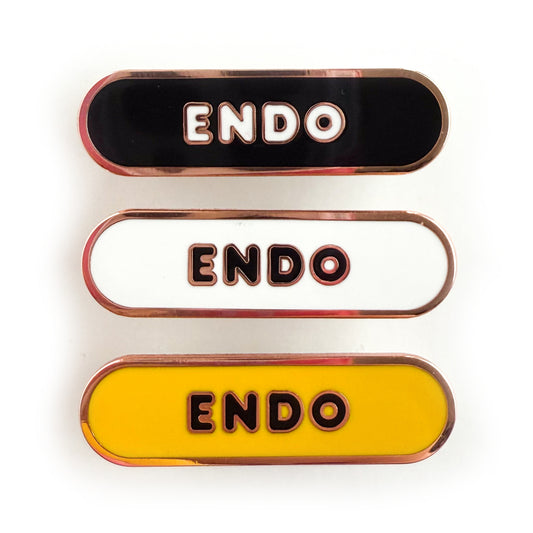 Three bandaid shaped pins with the text ENDO in bubble letters. Top one black with white text, the next is white with black text, and the last is yellow with black text.