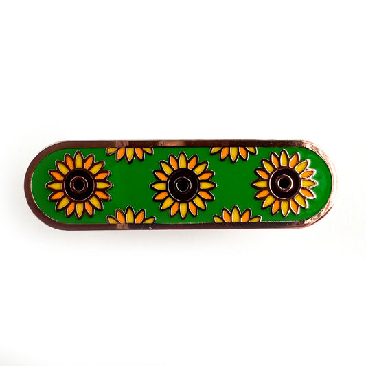 A capsule shaped pin with illustrations of sunflowers on a green background representing invisible disabilities.