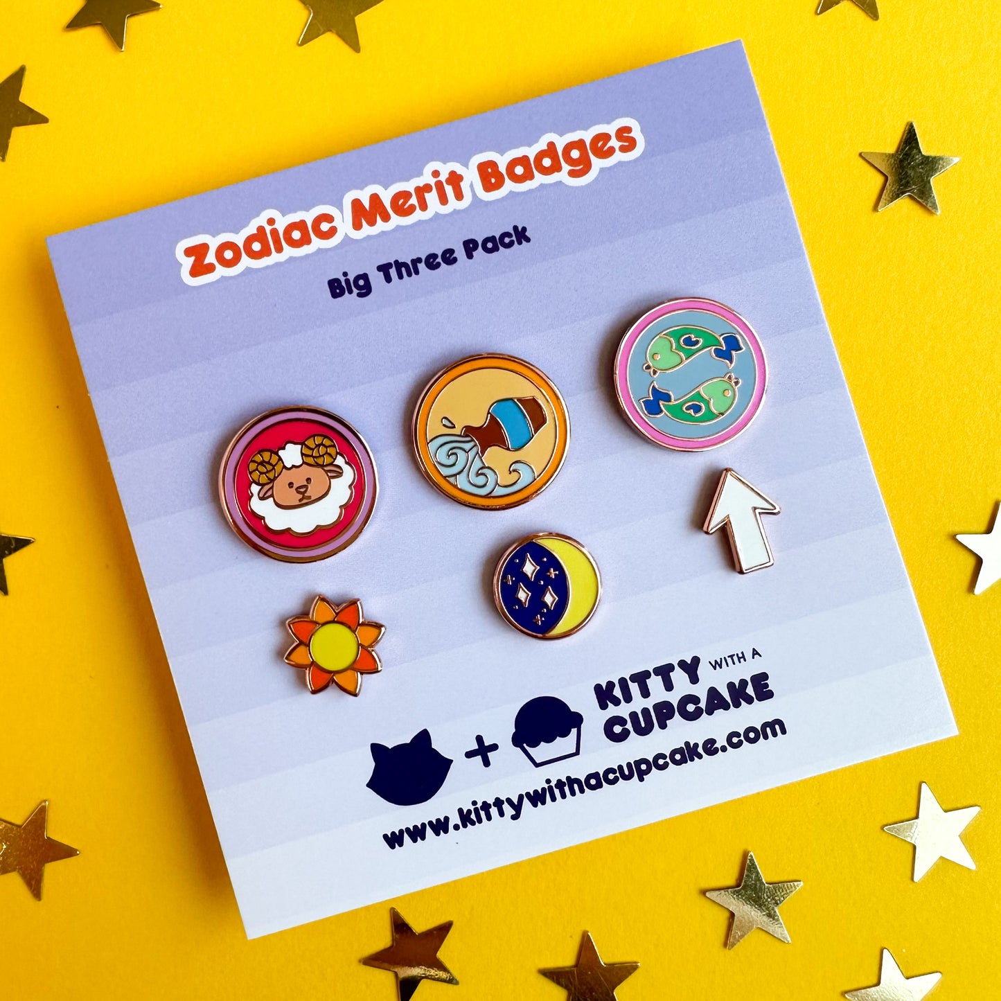 A set of six enamel pins, three are circles with cute illustrations representing zodiac signs. and the other three are shaped like a sun, moon, and rising arrow.  The pins are packaged on a card that reads "Zodiac Merit Badges"