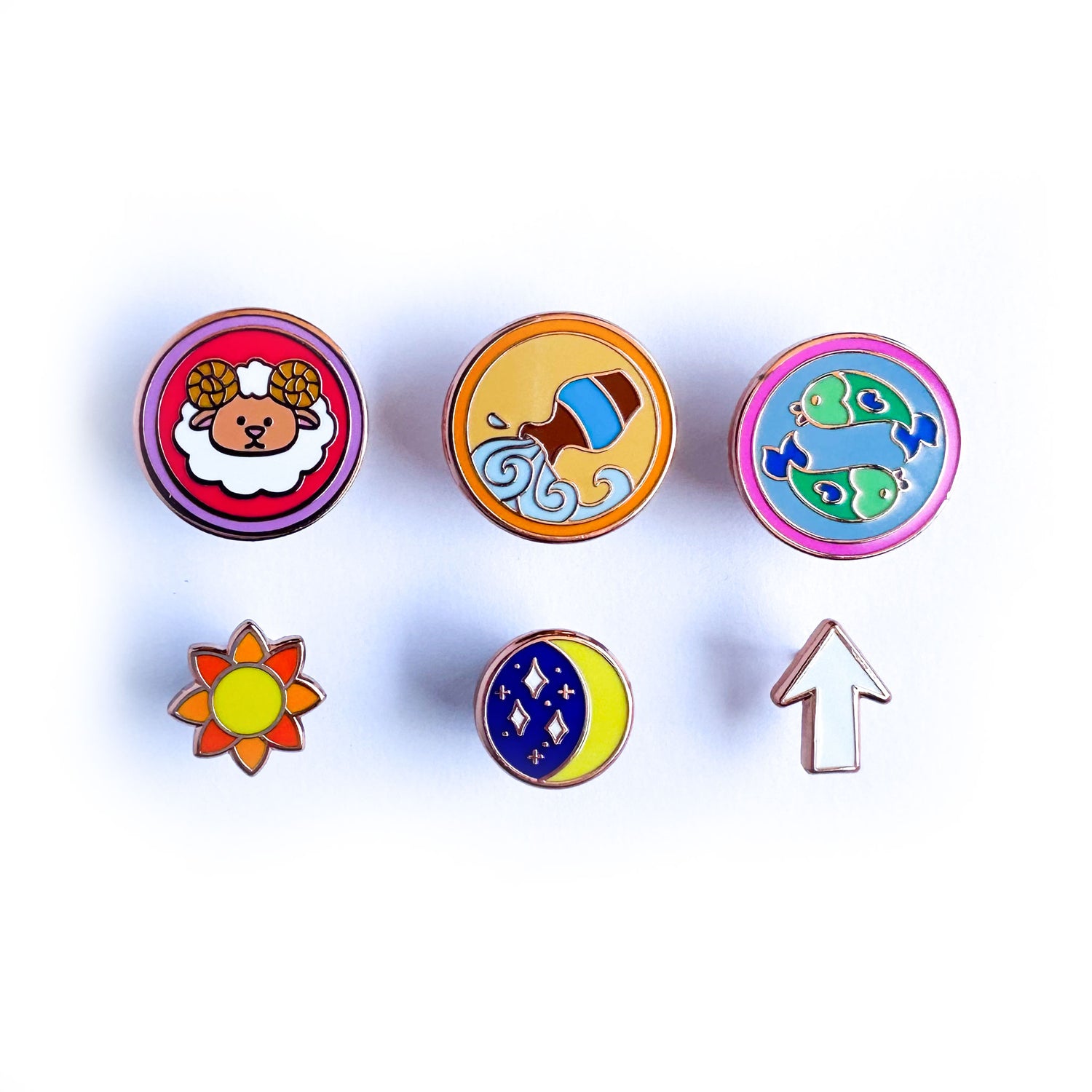 A set of six enamel pins, three are circles with cute illustrations representing zodiac signs. and the other three are shaped like a sun, moon, and rising arrow. 
