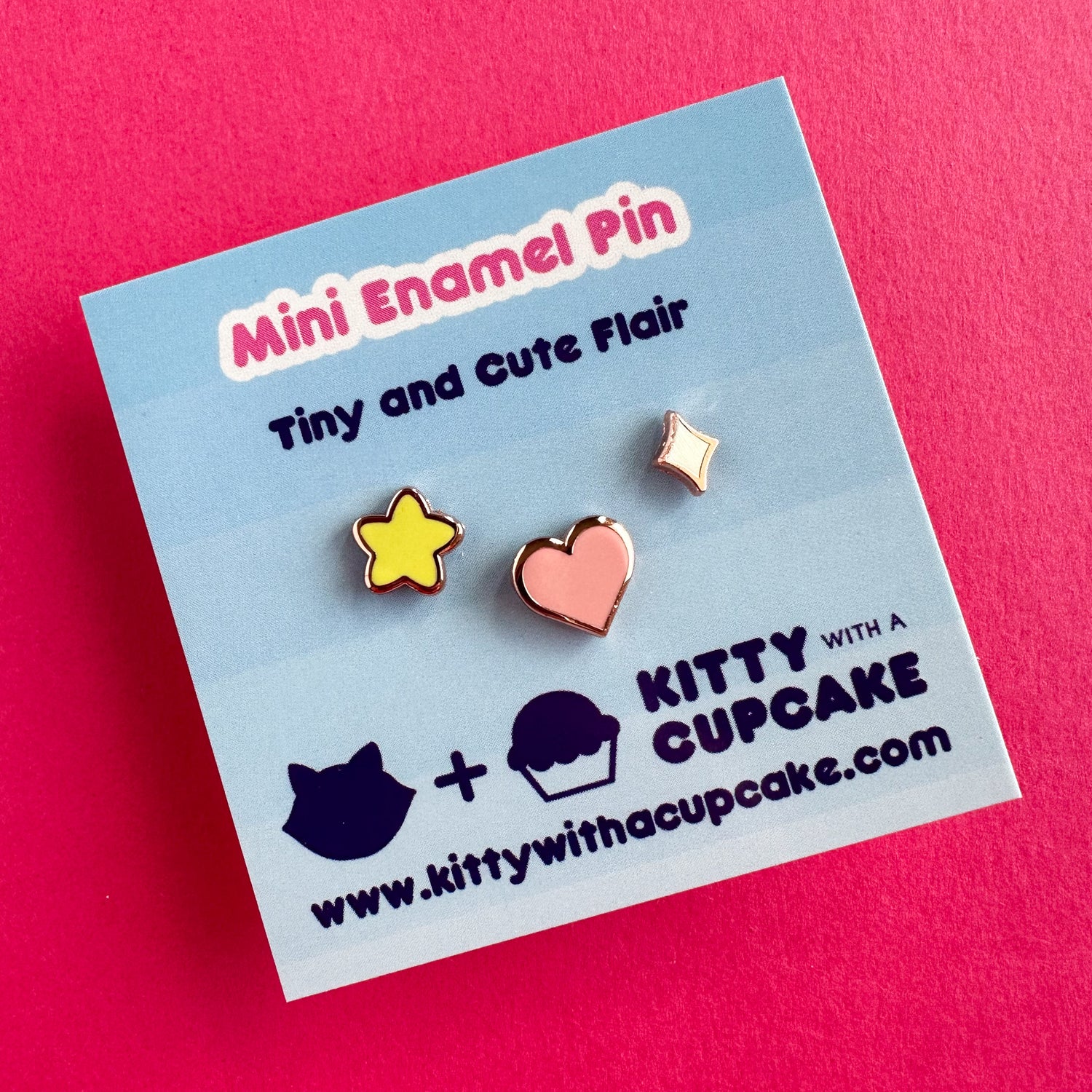 A square card with three enamel pins packaged on it. The card reads "mini Enamel pin - Tiny and Cute Flair". The pins are three different shapes, a yellow puffy star, a pink heart and a diamond sparkle. 