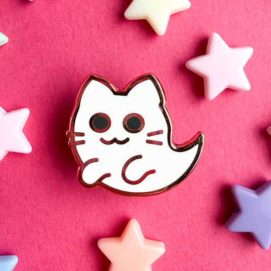 An enamel pin in the shape of a cute kitty ghost, the pin is on a hot pink background with plastic star beads around it.