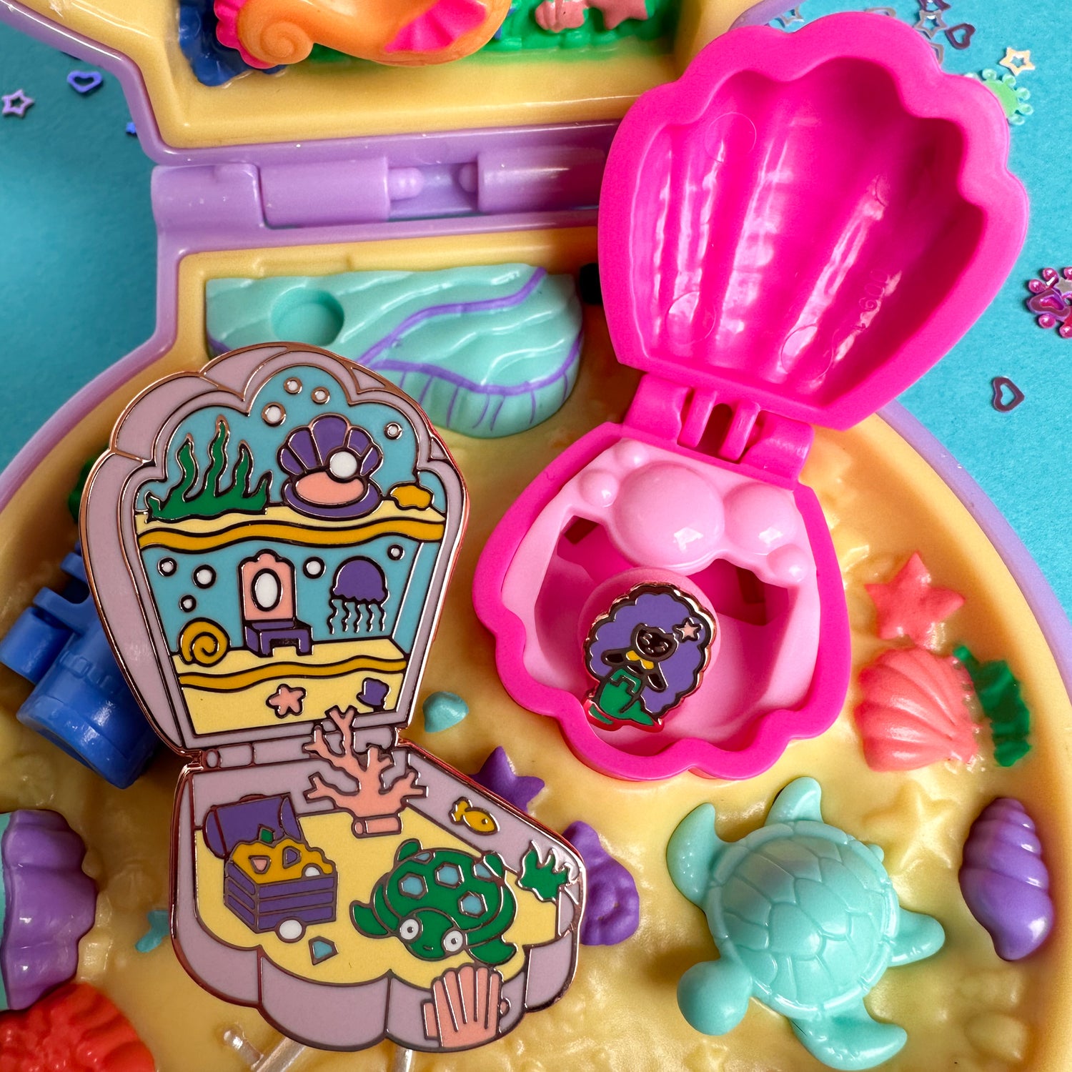The mermaid pocket pin set resting in a real Polly Pocket mermaid set. The mermaid pin is inside a pink plastic shell.