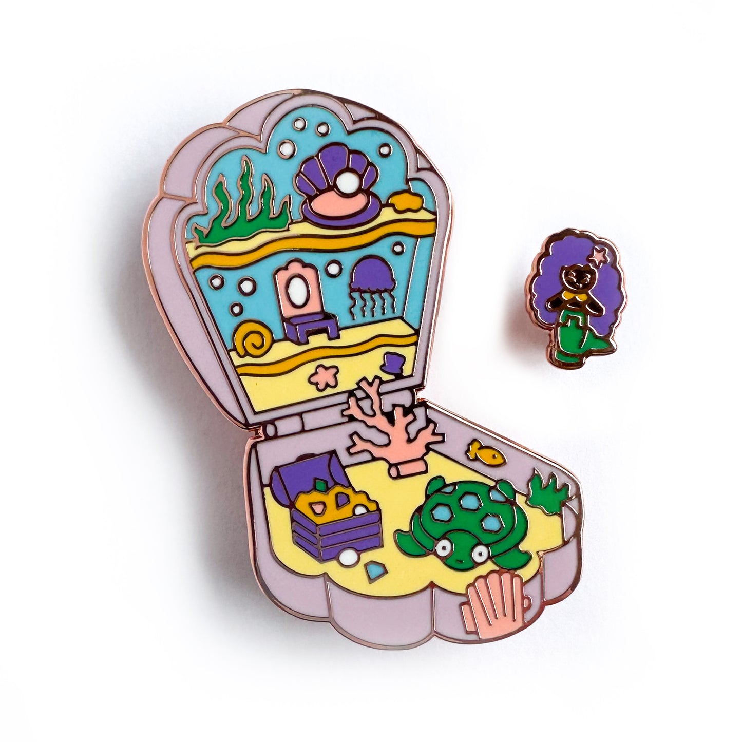 An enamel pin in the shape of a Polly Pocket compact shell with a mermaid mini pin. The shell compact is the mermaid's home with a jellyfish, coral, treasure chest, and a turtle.