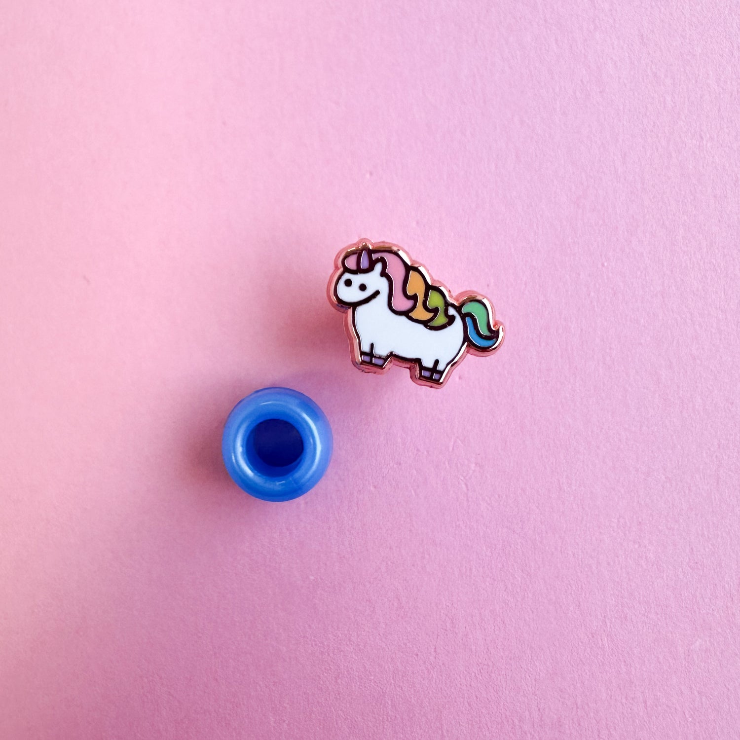 A mini unicorn pin with a blue plastic pony bead next to it for scale. 