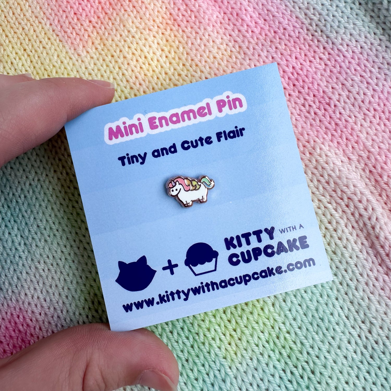 A hand holding a small square card with a itty bitty unicorn pin on it. The card reads "Mini Enamel Pin - Tiny and Cute Flair"