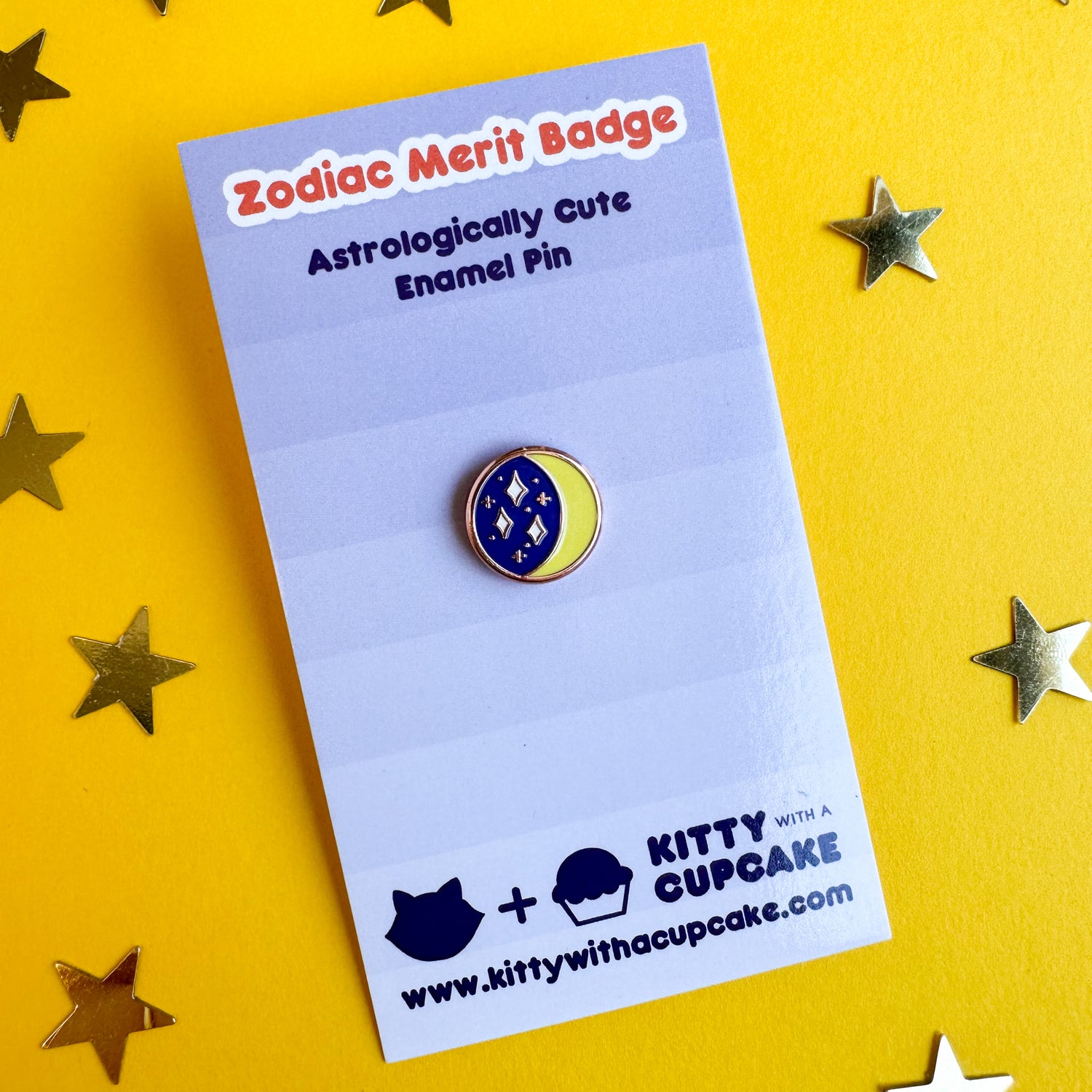 A circular enamel pin of a crescent moon with a starry sky packaged on a periwinkle card that reads "Zodiac Merit Badge" across the top. This is sitting on a yellow background with gold star confetti around it. 
