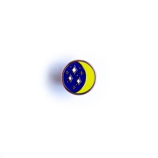 A circular enamel pin with an image of a crescent moon and a starry sky inside it.