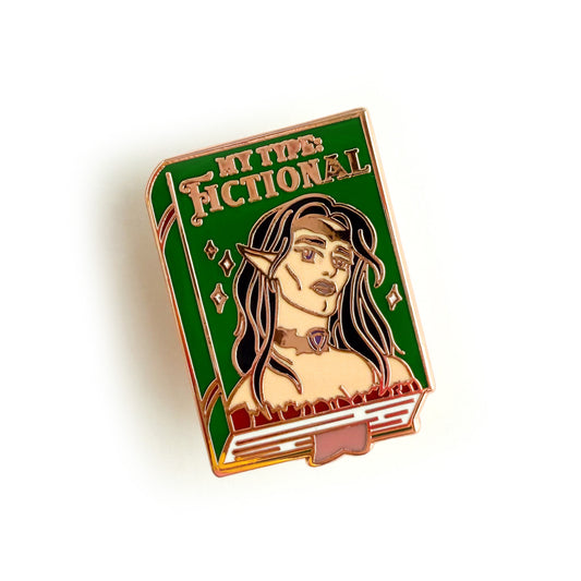 An enamel pin depicting a green book with the title “My Type: Fictional” written in gold. There is a hot androgynous elf on the cover with long black hair, big purple eyes, and luscious pink lips. They have sharp features, high cheek bones, and a chiseled jaw. They are wearing a gold crown, a gold choker with a purple gem, and an off-the-shoulder brown top. The book has gold accents on the spine, white sparkles on the cover, and a pink bookmark sticking out of the bottom.