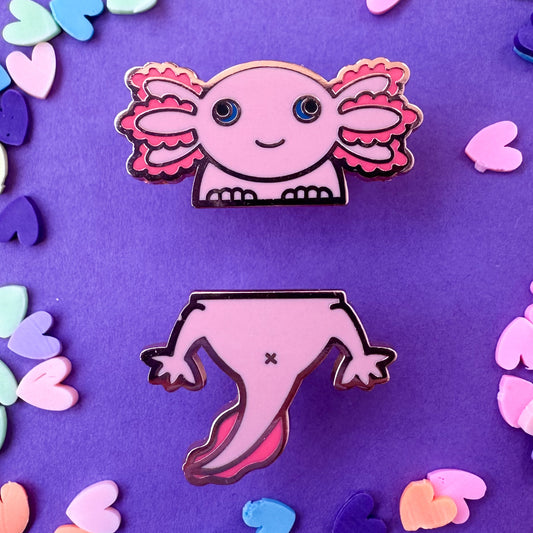 Two pins representing the top and bottom half of an axolotl, one is the face that is smiling and the other is the bottom with the tail. The pins are on a purple background with pastel heart sprinkles around. 