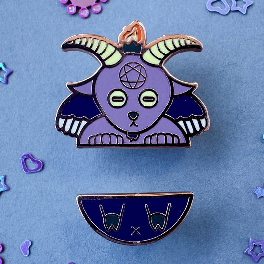 A set of two pins forming Baphomet, one is the top half with the head and the other is the bottom. The pins are on a grey background with glitter around it,