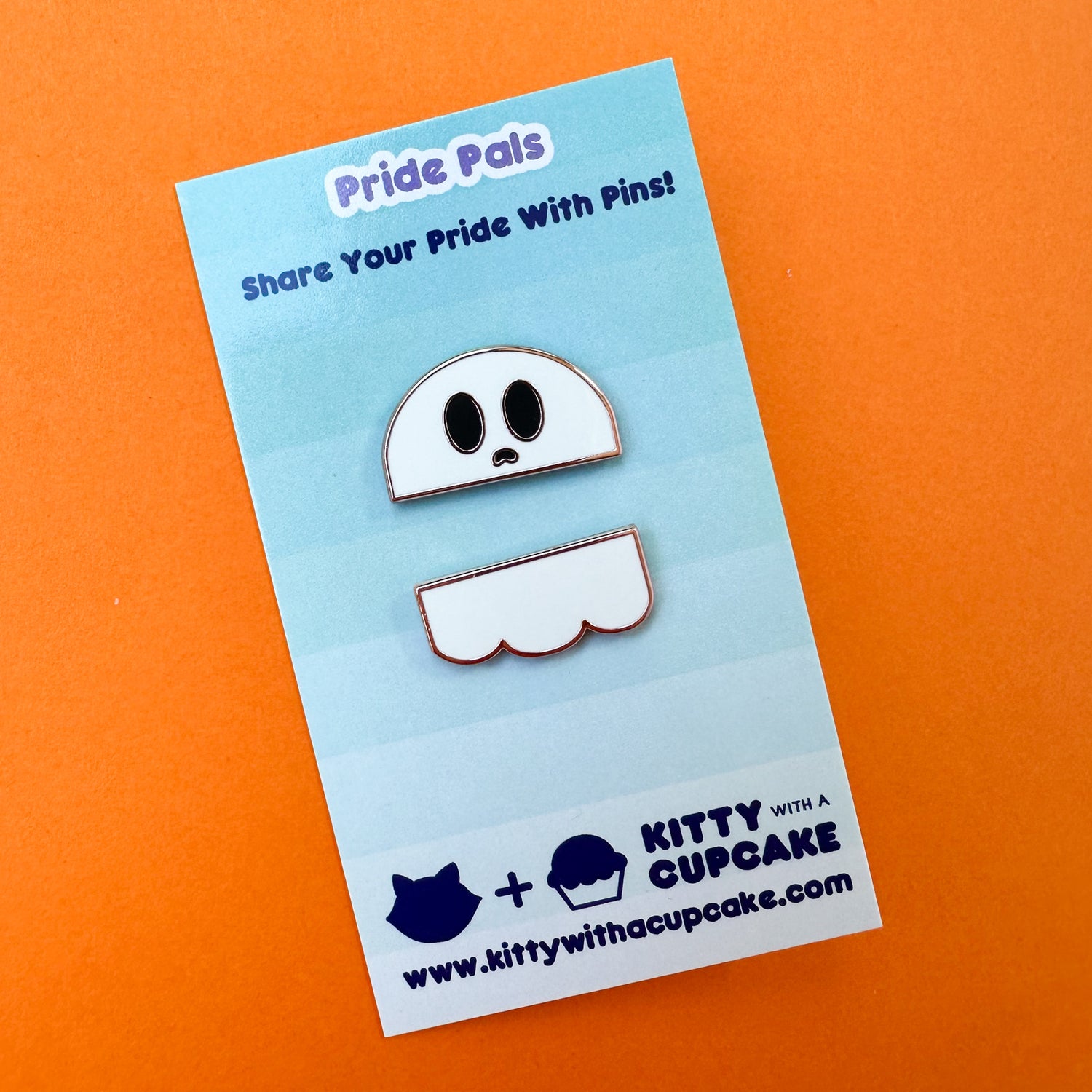 Two enamel pins that come together to form a ghost, they are packaged on a card which is sitting on an orange background. 