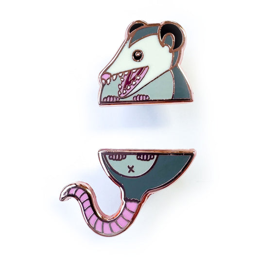 Two enamel pins that come together in the middle to form an opossum, the top pin is the head and the bottom is the butt and tail.