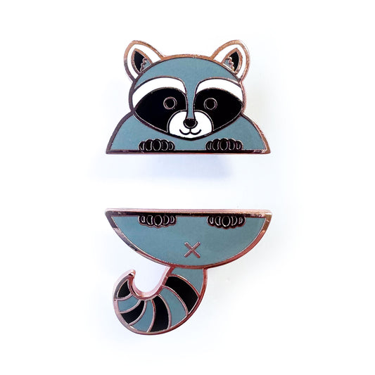 Two enamel pins that come together in the middle to form a cute raccoon, the top pin is the head and front paws and the bottom pin is the tail and back paws. 