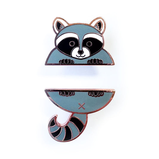 Two enamel pins that come together in the middle to form a cute raccoon, the top pin is the head and front paws and the bottom pin is the tail and back paws.