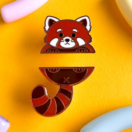 A two piece pin set that comes together to form a red panda. The top pin is the red panda’s top paws and head. The bottom pin is the red panda’s butt, stripped tail, and feet. The pins are on a yellow background.