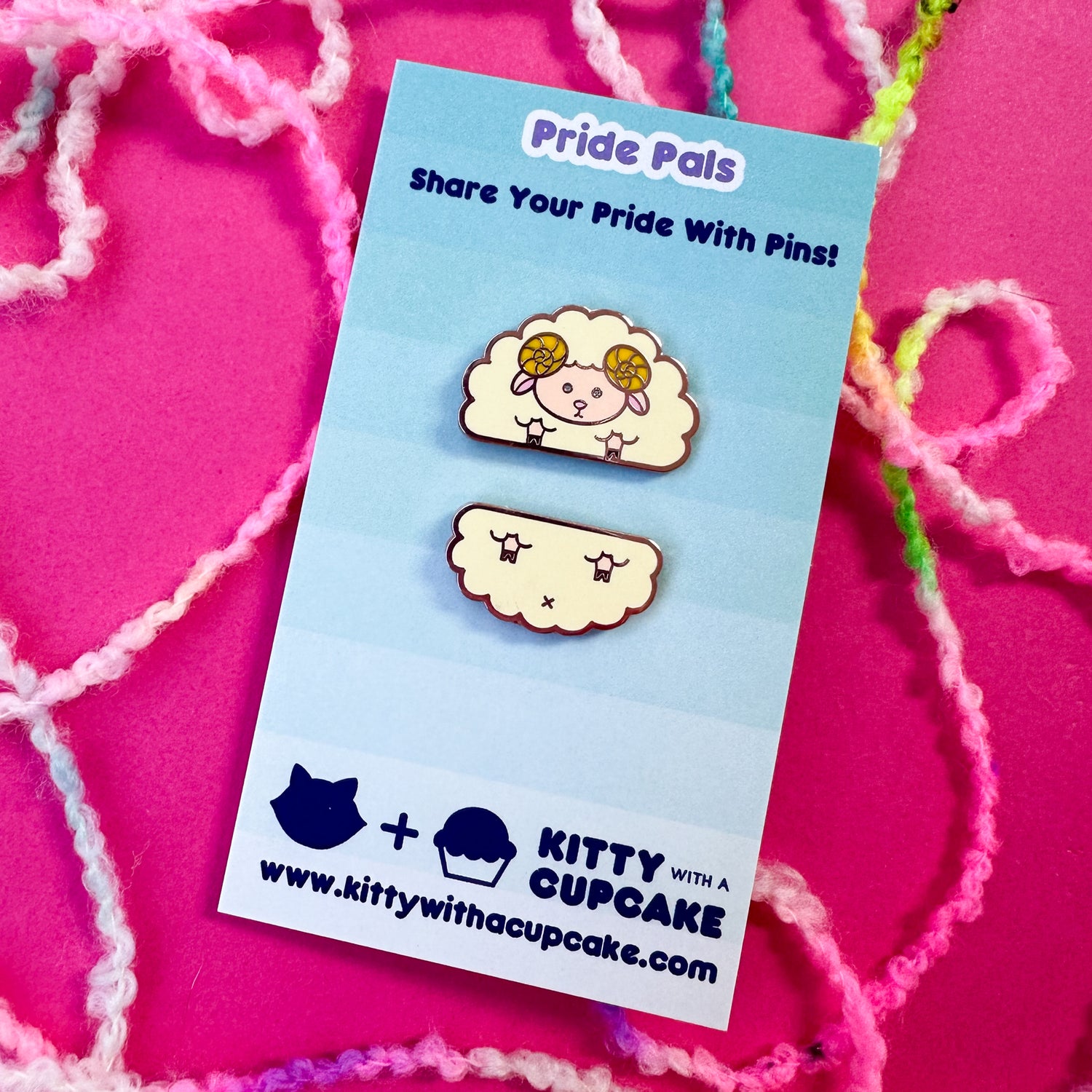 Two cute enamel pins that come together to form a sheep packaged on a blue card on top of a hot pink background with boucle yarn around it. 