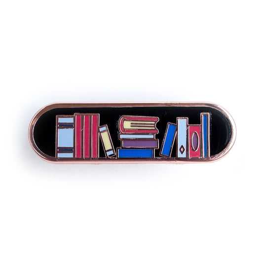 An enamel pin in the shape of a bandaid with books stacked in it like a bookshelf, the background of the pin is black and the books are red, blue, and purple.