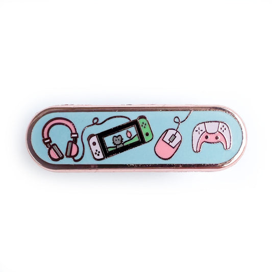 A capsule shaped pin with a light blue background and illustrations of a Nintendo Switch, a Playstation controller, a computer mouse and headphones on it. The game systems are in pastel pink colors.