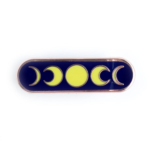 A capsule shaped pin with a dark blue background with yellow illustrations of moon phases on it. 
