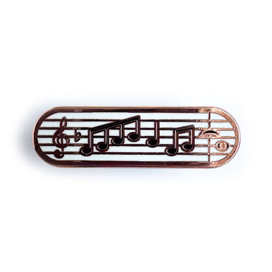A capsule shaped enamel pin with a music staff with a treble clef and music notes on it.