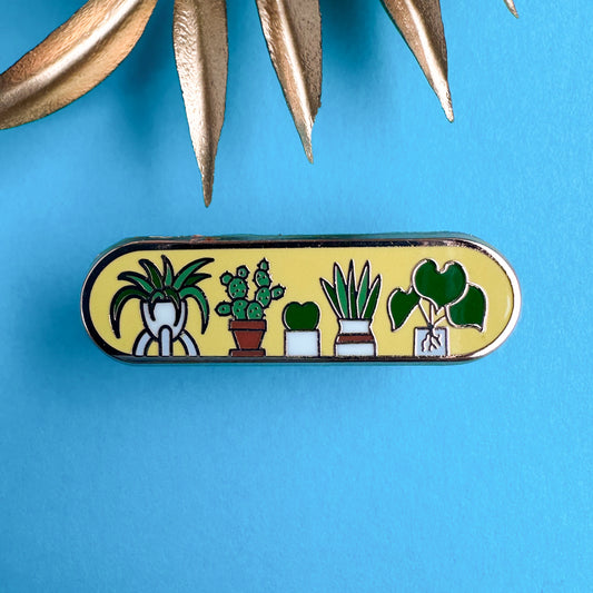 An oval shaped pin with illustrations of cute house plants like a cactus, spider plant, Hoya, and snake plant on it. The pin is on a blue background with some gold leaves in the background.