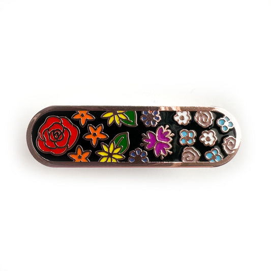 An oval shaped pin with flowers on it in the colors of the rainbow and trans pride flags.