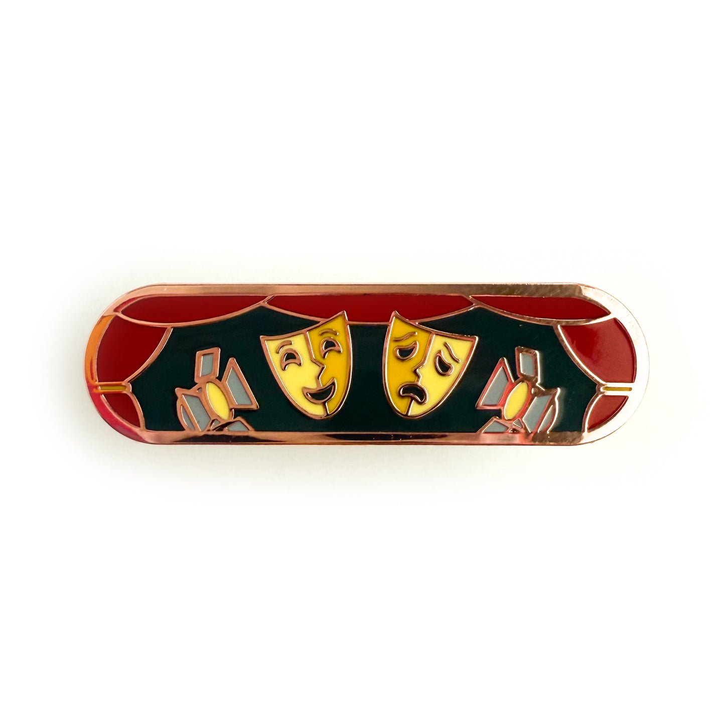 A bandaid shaped enamel pin with theater themed illustrations. There is a red curtain boarder around both a comedy and tragedy mask and two stage lights.