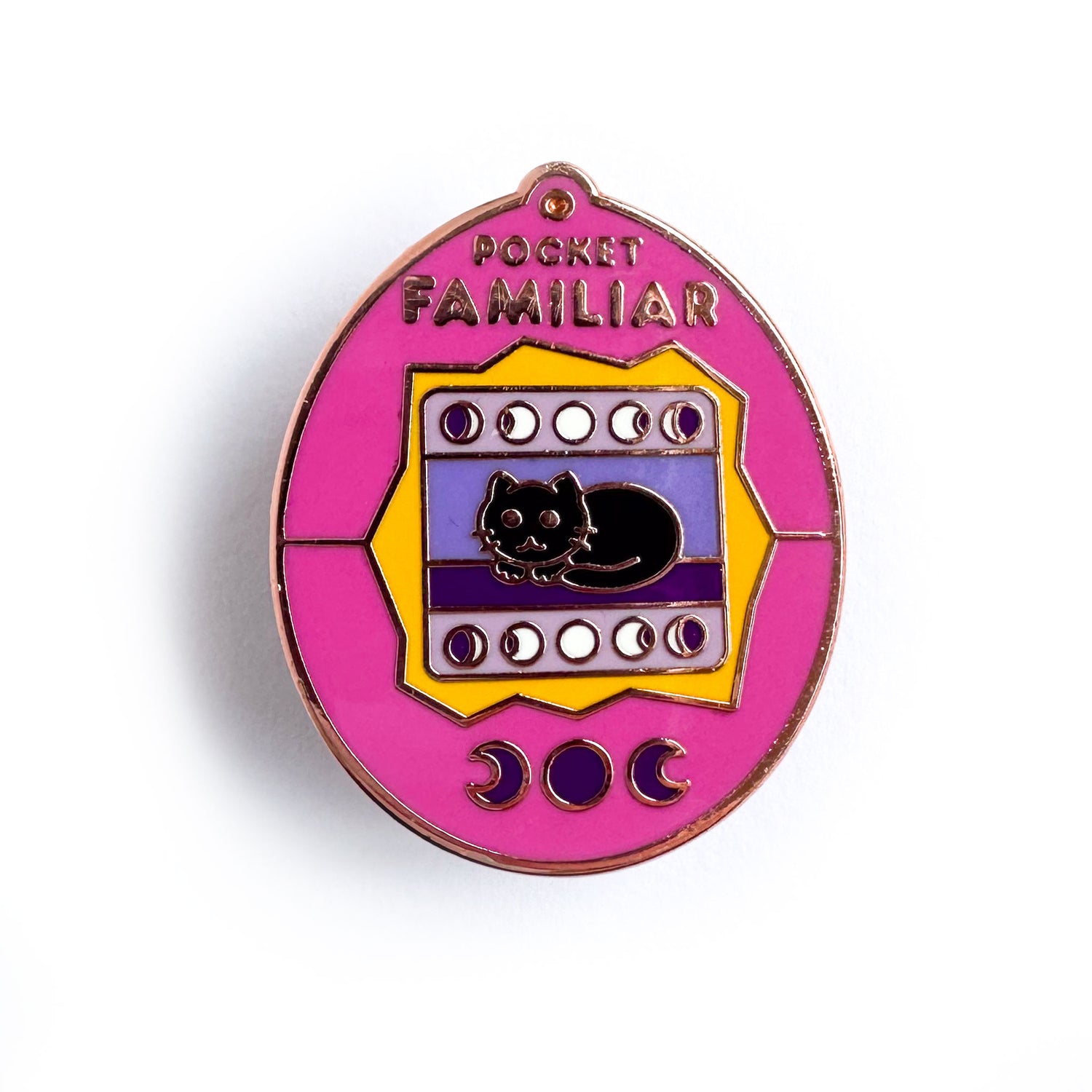 An enamel pin in the shape of a tamagotchi virtual pet. It has a black cat on the screen and reads "Pocket Familiar" across the top. It is a pink shell with yellow details.